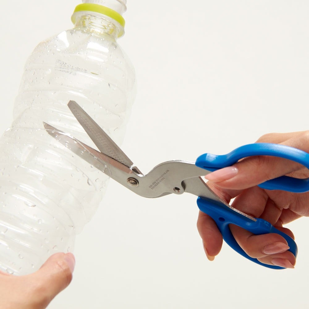 Multi-purpose scissors cutting a clear PET plastic bottle